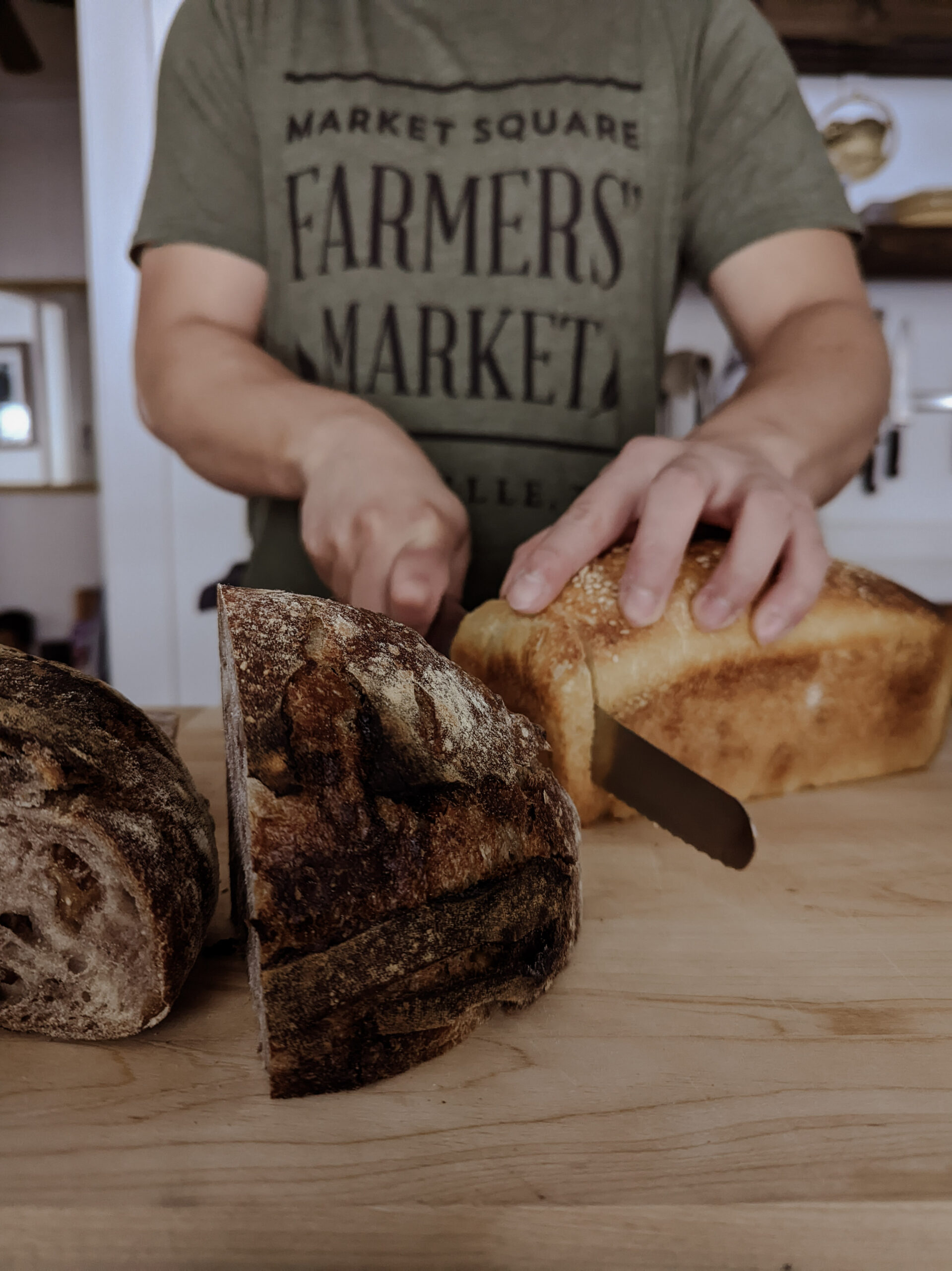 Chef Sal in Farmers Market shirt slicing sourdough loaves