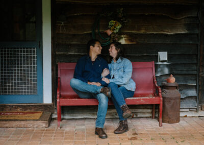 Amber and Sal on a vintage red bench in front of 1860s log cabin